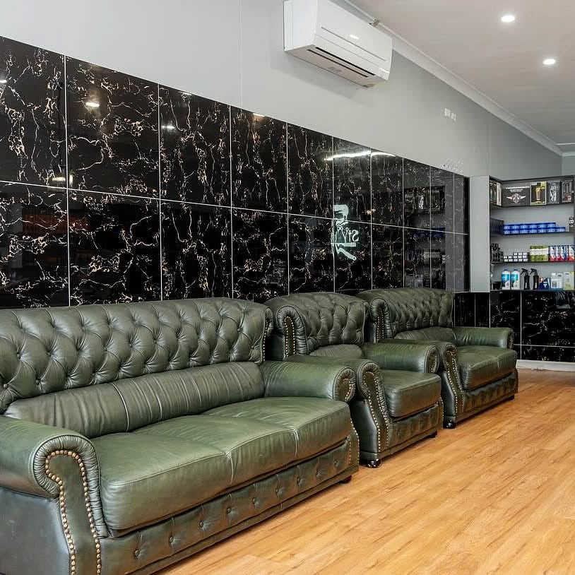 Green leather chesterfield lounges and black marble wall inside STYLO Barbershop